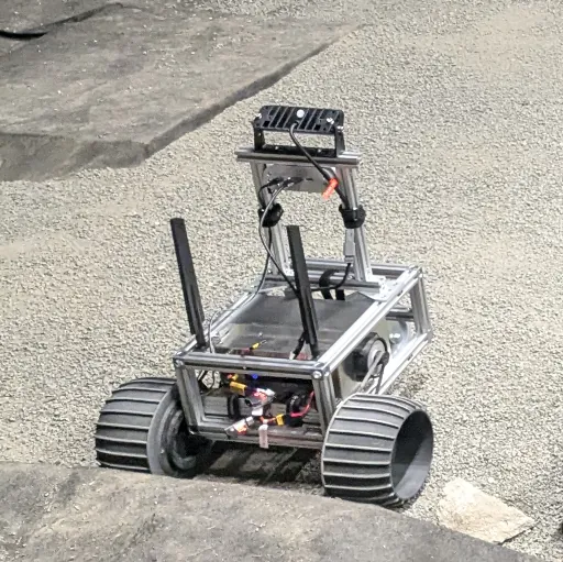 A rover with treaded wheels driving over sandy analogue terrain
